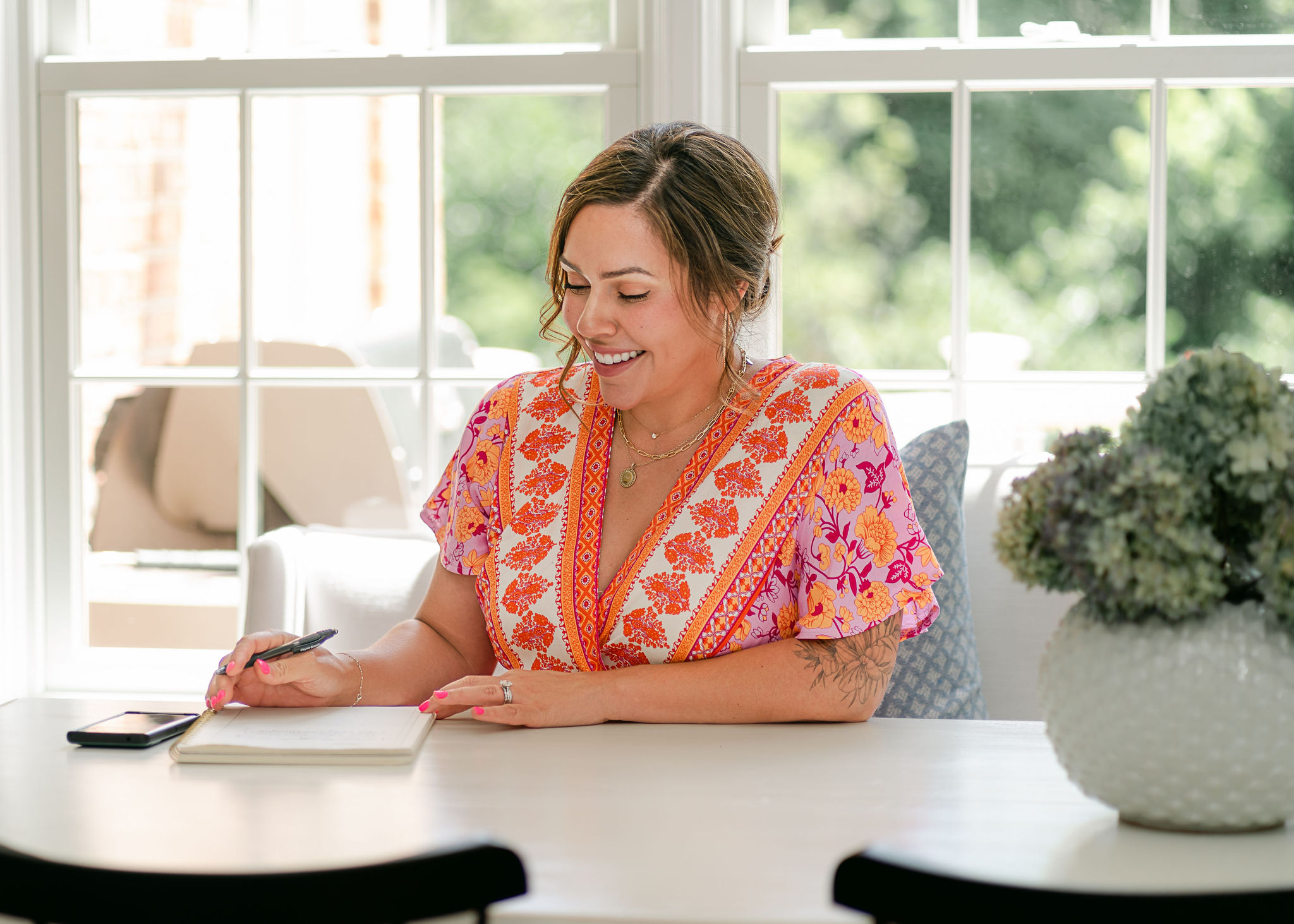 woman at white kitchen table writing in a journal and smiling